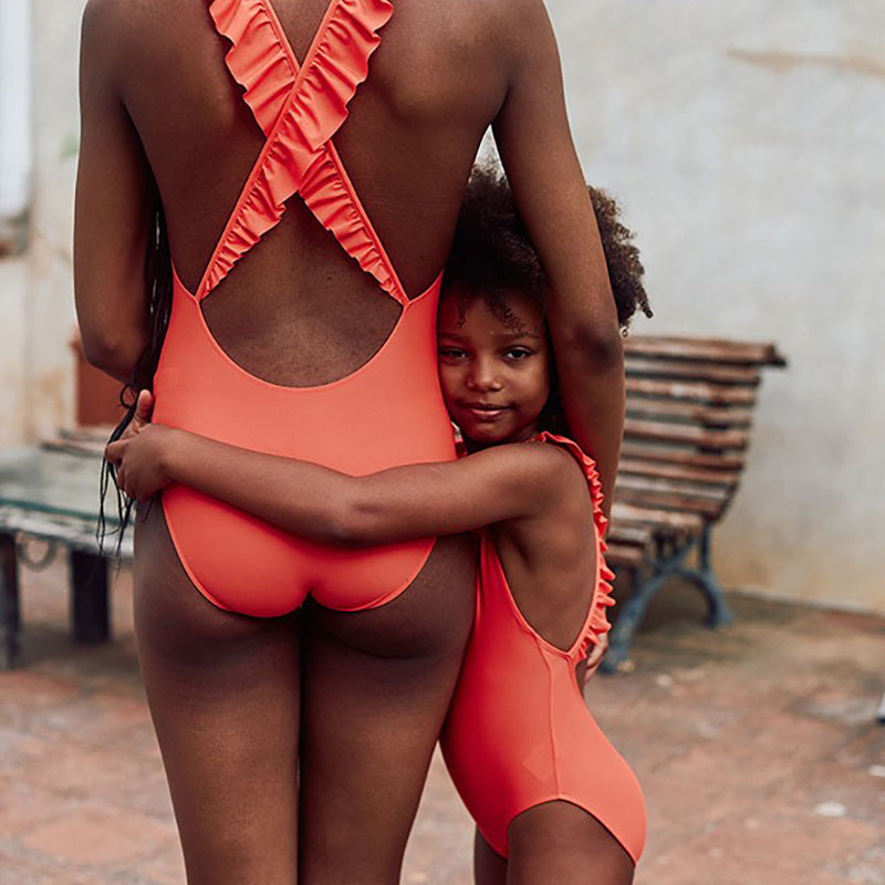 Little girl wearing bright red one-piece swimsuit with ruffles on the back