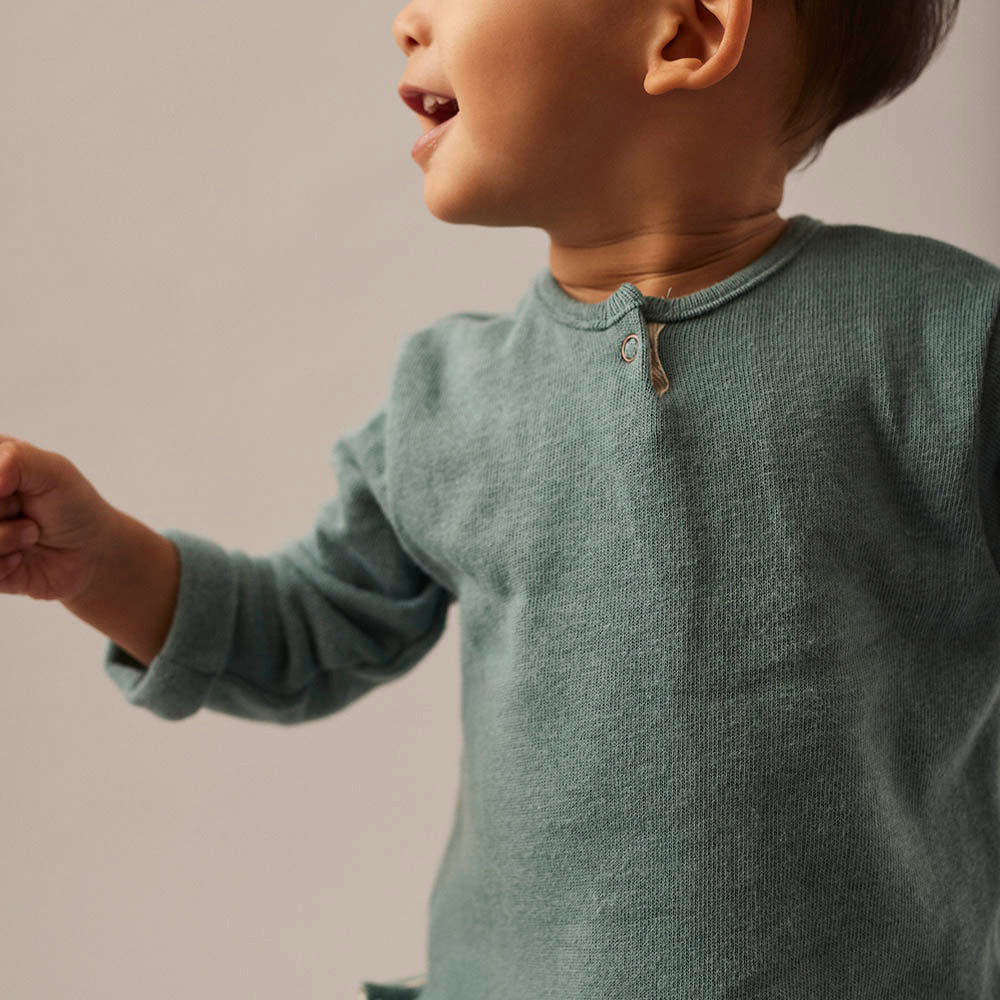 Child wearing a green long-sleeve shirt against a neutral background